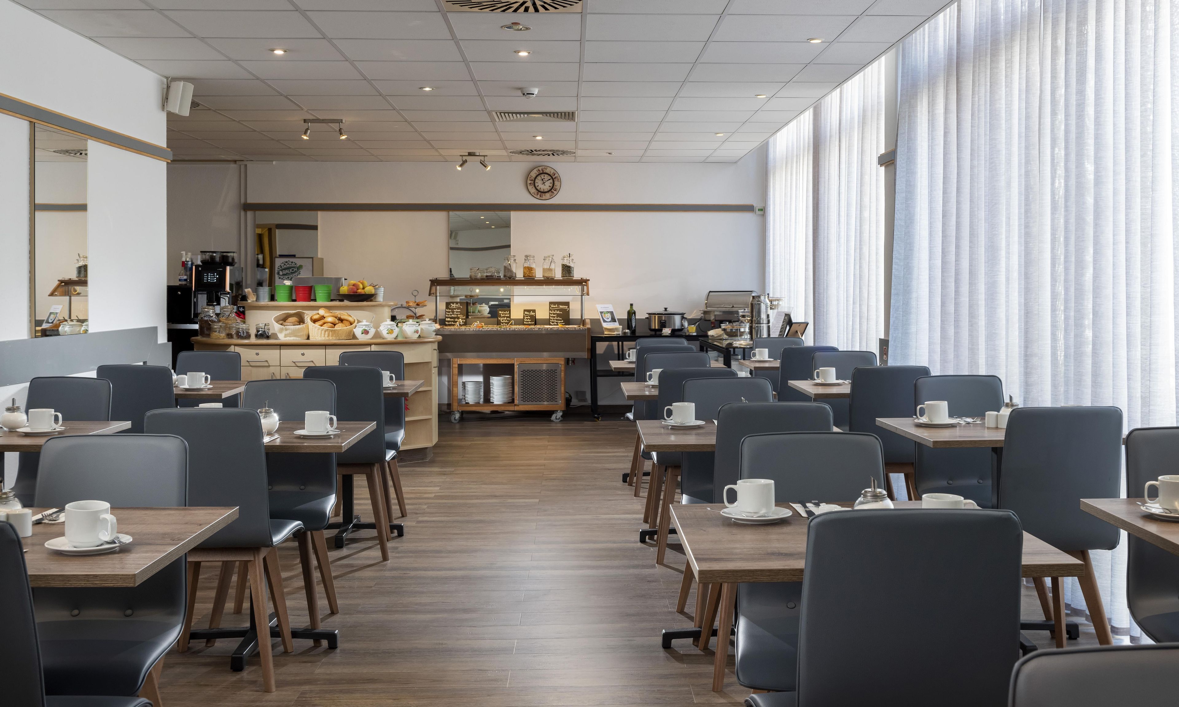 A modern cafe with a long counter, seating area, and a kitchen in the background.