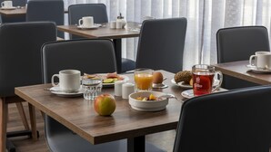 Ein Frühstückstisch für zwei Personen, mit einer Kaffeetasse, einem Orangensaftglas, einer Obstschale und einem Teeglas.