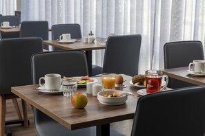 Ein Frühstückstisch für zwei Personen, mit einer Kaffeetasse, einem Orangensaftglas, einer Obstschale und einem Teeglas.