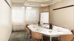 Un salón de conferencias con una larga mesa, sillas, una pantalla de proyector y una estación de café.