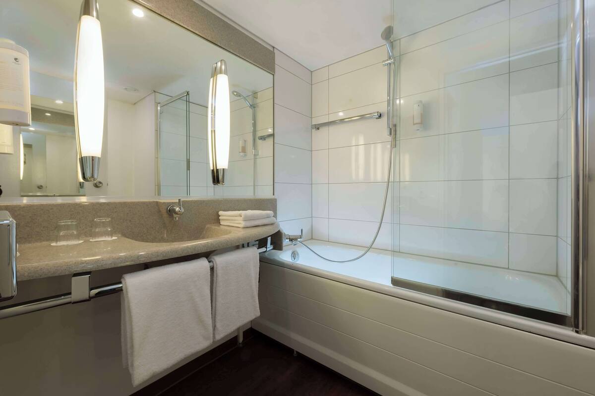 A modern bathroom with a large mirror, a bathtub, and a shower.