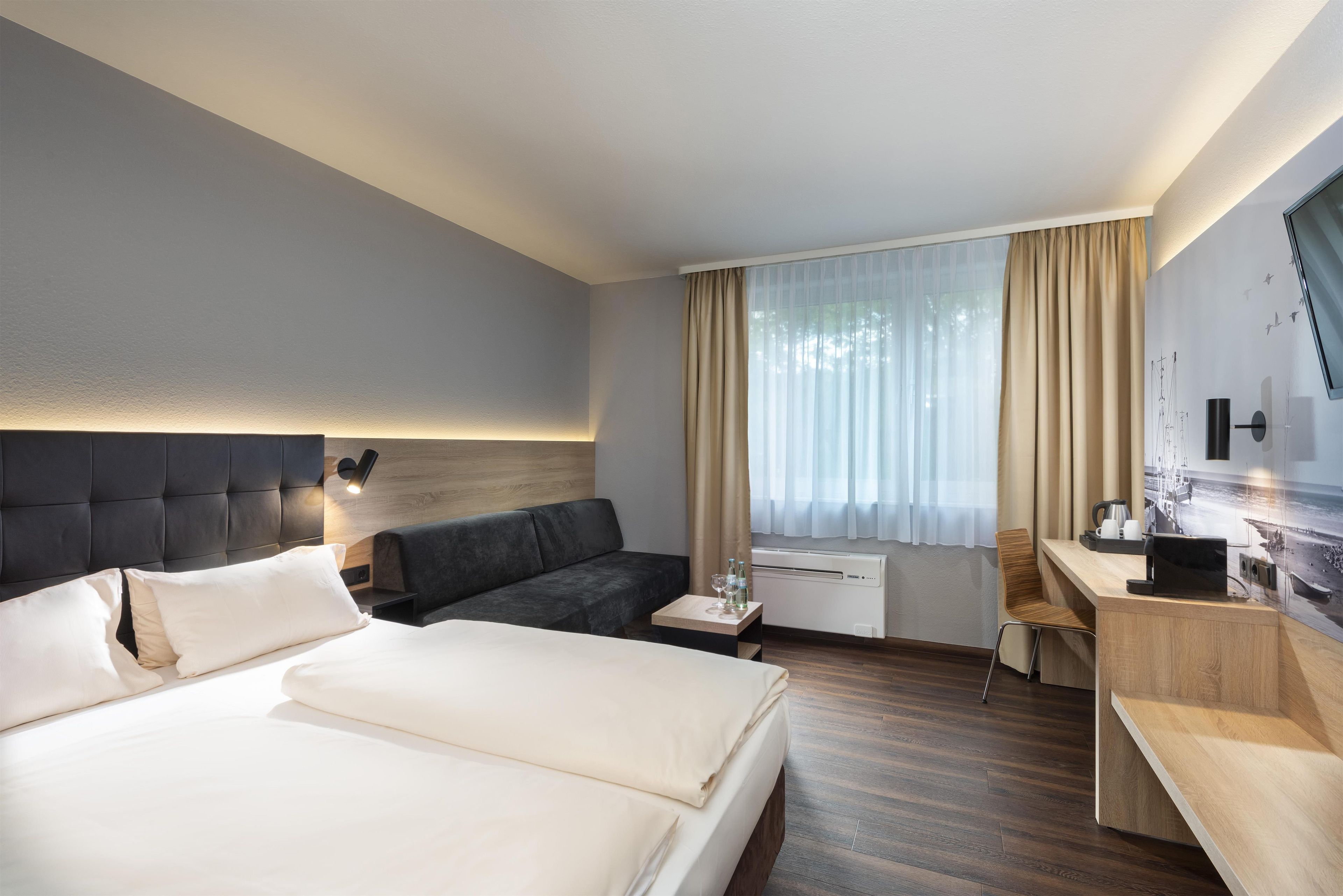 A hotel room with a bed, a sofa, a desk, and a window with curtains.