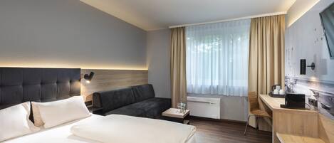Habitación de hotel con cama, sofá, escritorio y ventana con cortinas.