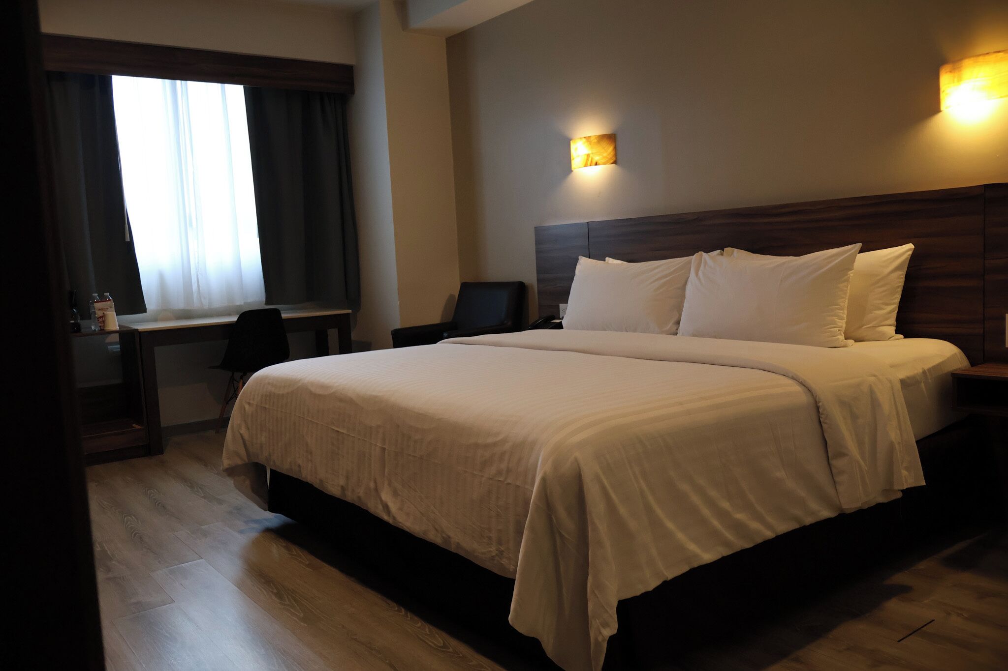 A hotel room with a large bed, a desk, a chair, and a window with curtains.