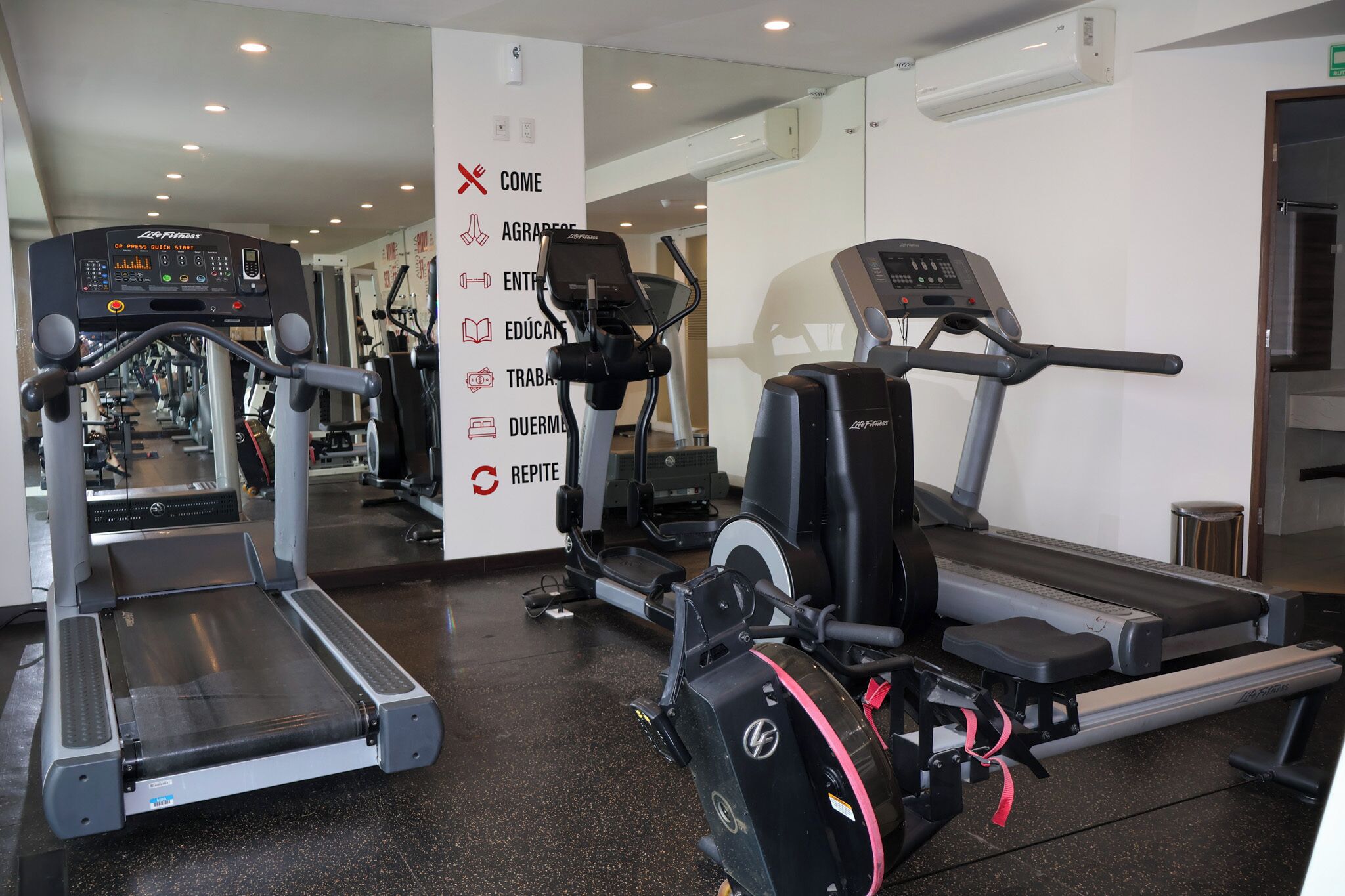 A gym with treadmills, ellipticals, and a mirrored wall.