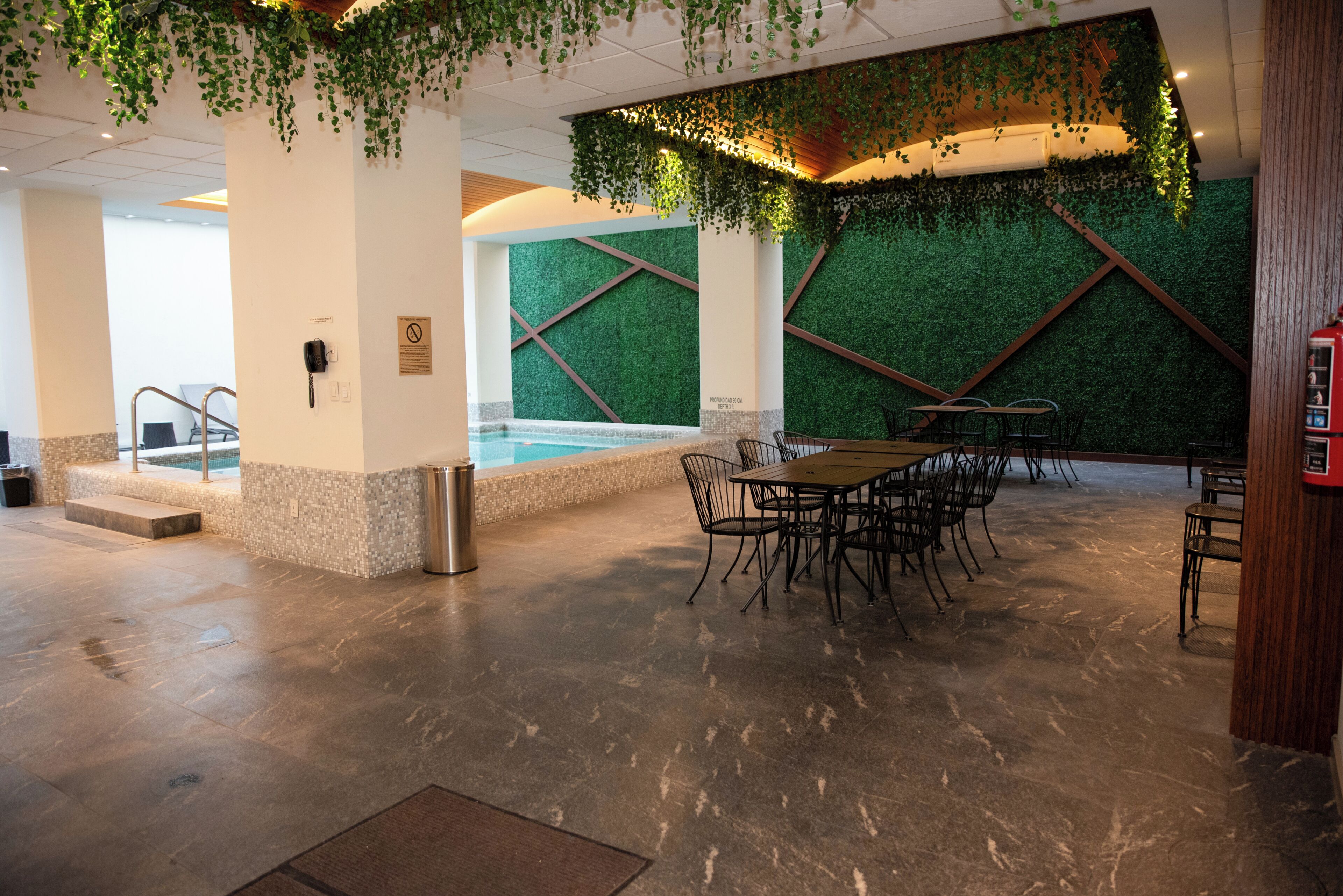 Zona de piscina con mesa y sillas, un cubo de basura y un teléfono en la pared.