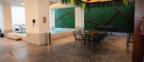 A pool area with a table and chairs, a trash can, and a phone on the wall.