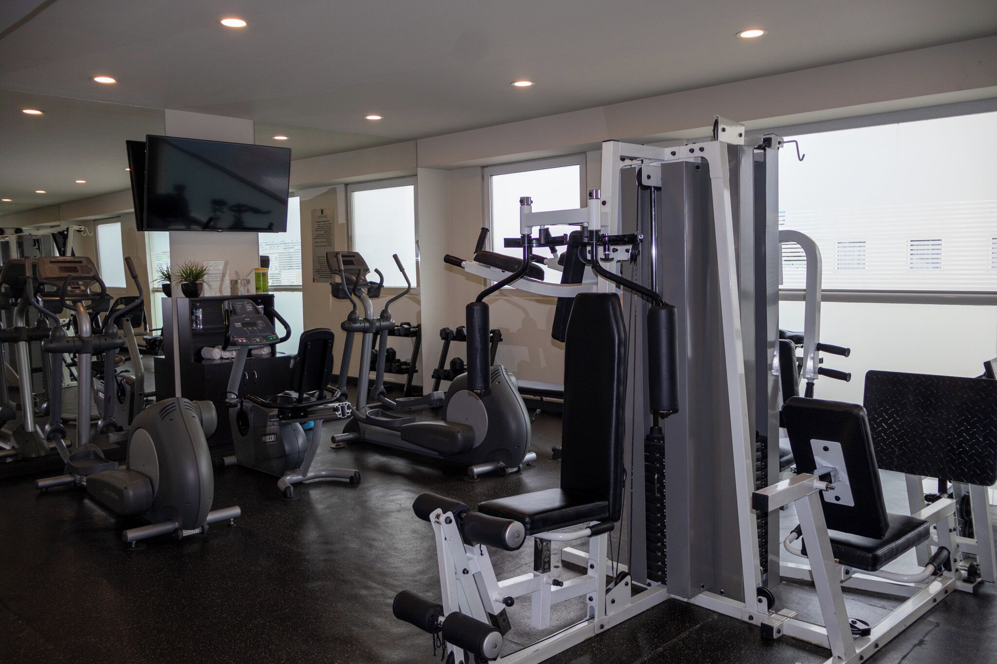 A gym with various exercise machines, a television, and large windows.