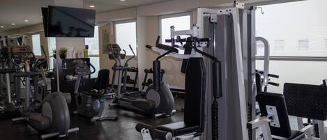 A gym with various exercise machines, a television, and large windows.