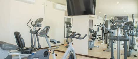 A gym with cardio machines, weight equipment, and a TV mounted on the wall.