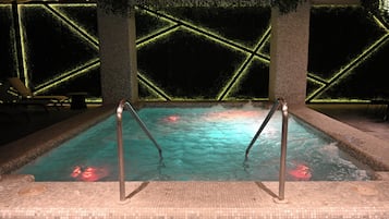 A hot tub with metal ladders, surrounded by tiled walls with geometric patterns and greenery.