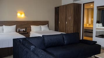 A hotel room with two beds, a dark sofa, a wardrobe, and a bathroom visible through an open door.
