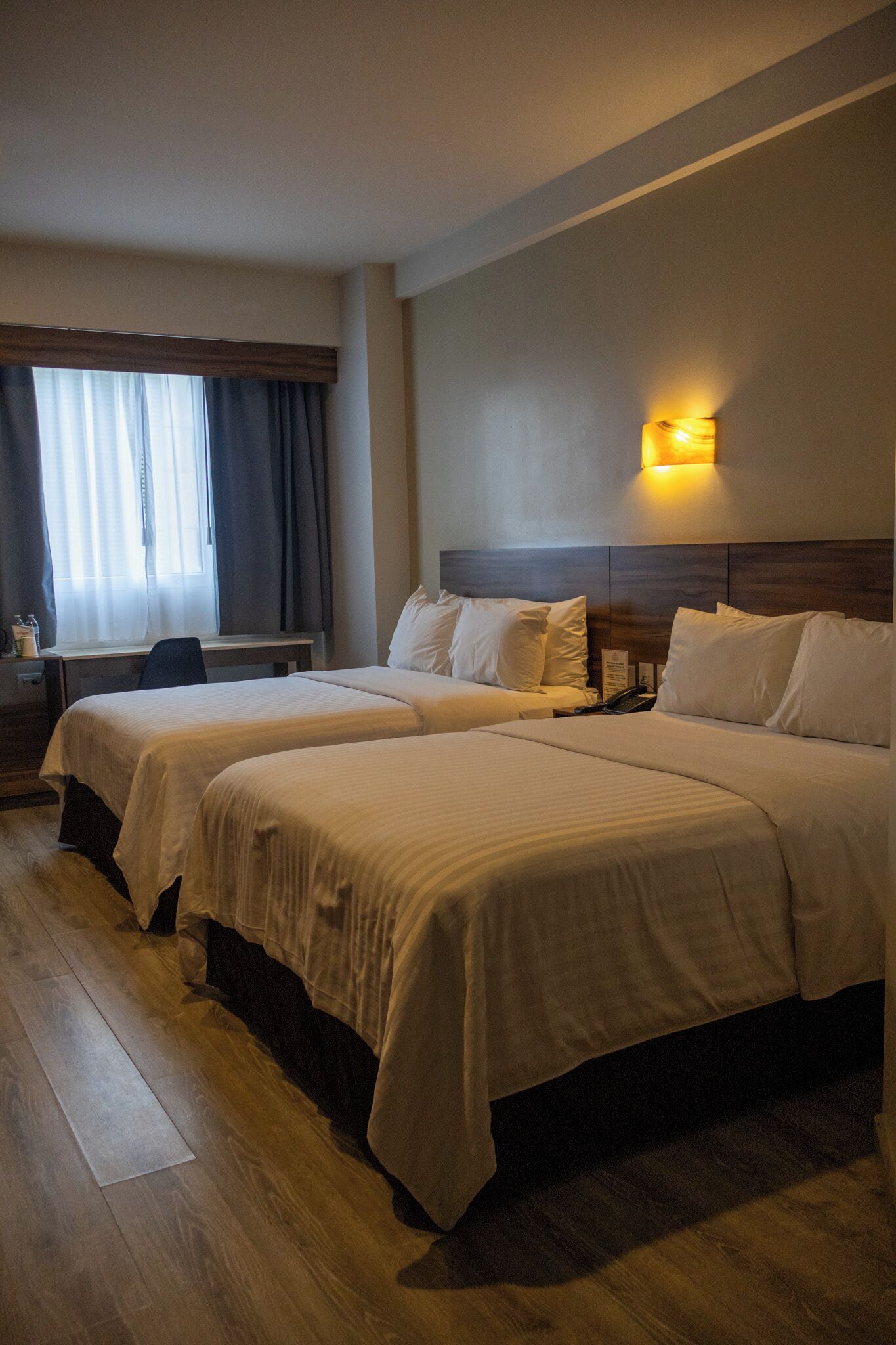 Une chambre d’hôtel avec deux lits, un bureau et une fenêtre avec des rideaux.