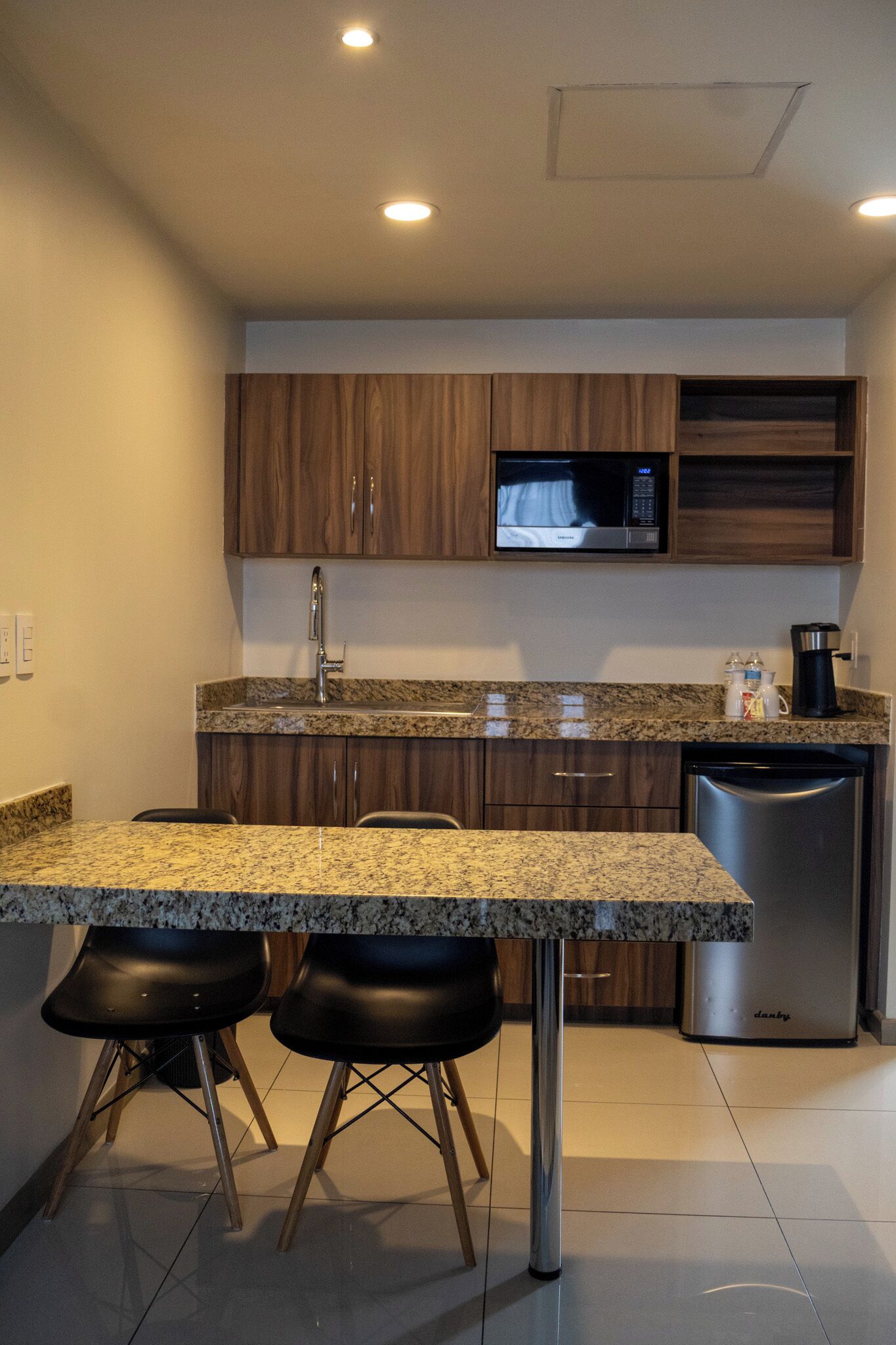 Una cocina con encimeras de granito, gabinetes de madera, lavavajillas de acero inoxidable y microondas.