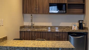 Una cocina con encimeras de granito, gabinetes de madera, lavavajillas de acero inoxidable y microondas.