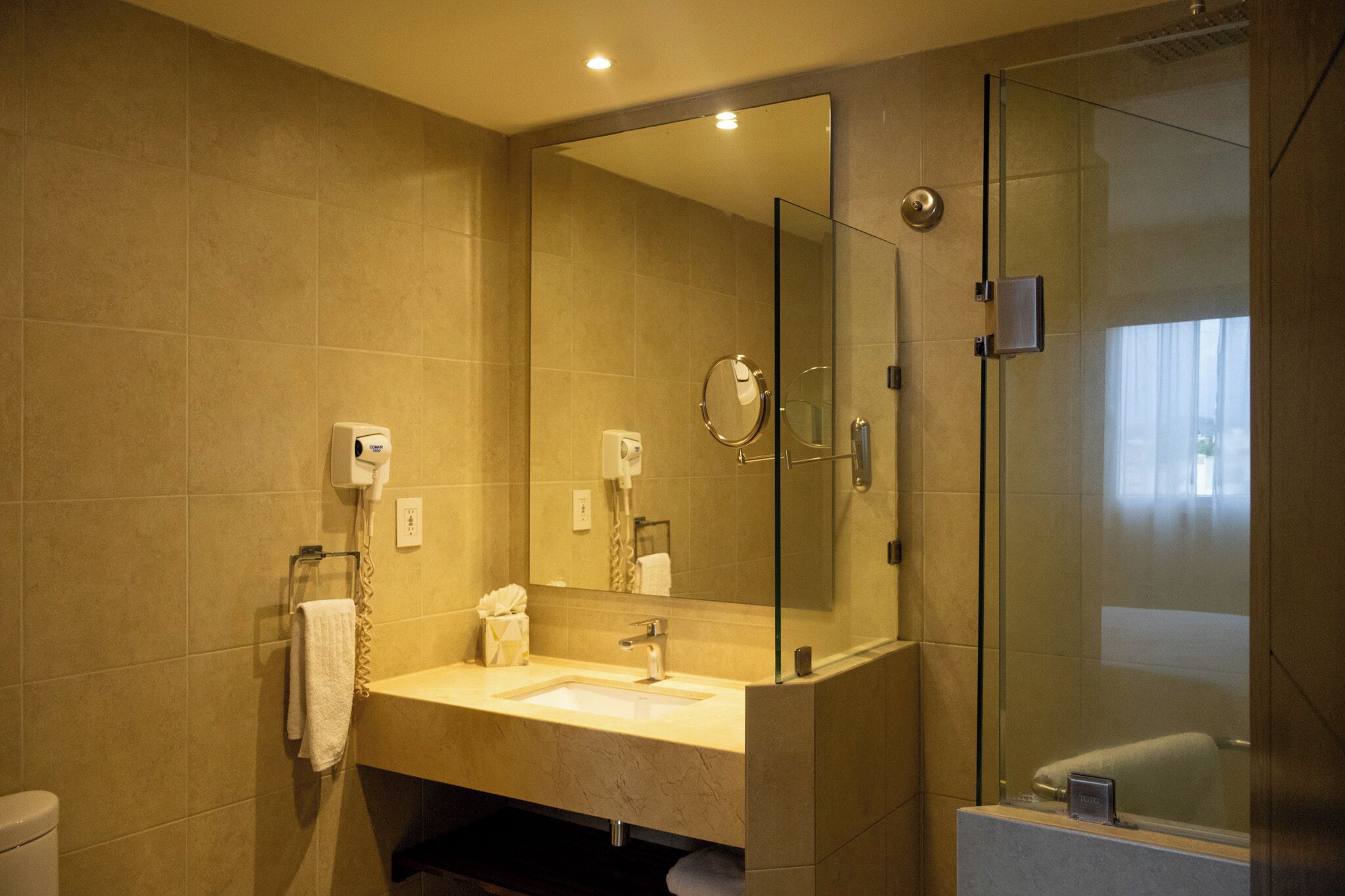 Un baño con ducha de mampara de vidrio, un lavamanos con espejo y un perchero para toallas.