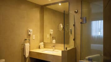 Un baño con ducha de mampara de vidrio, un lavamanos con espejo y un perchero para toallas.