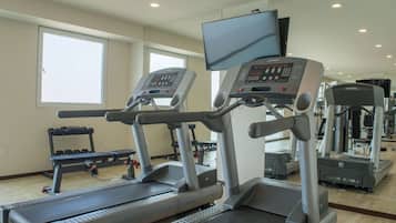 Une salle de sport équipée de tapis de course, d’haltères et d’un téléviseur fixé au mur.