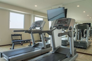 Ein Fitnessstudio mit Laufbändern, Hanteln und einem an der Wand befestigten Fernseher.