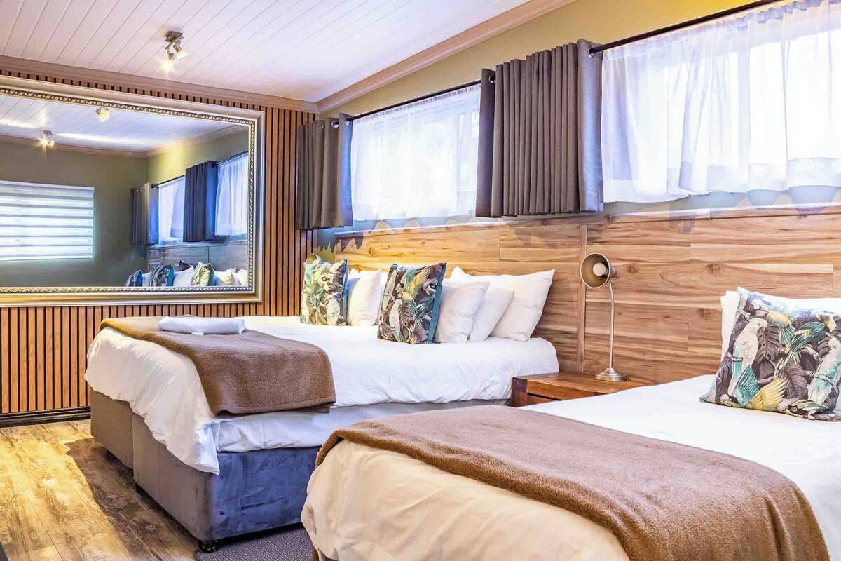 A hotel room with two beds, a large mirror, wooden paneling, and a window with curtains.