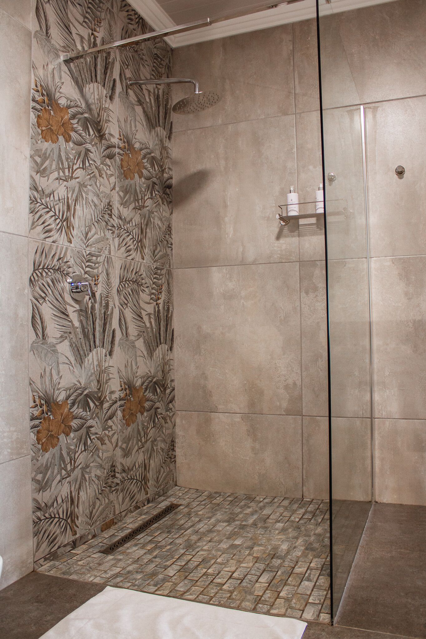A walk-in shower with a tiled floor and a floral wall design.