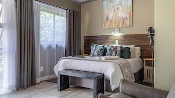A bedroom with a large bed, a bench, a bedside table, and a painting on the wall.
