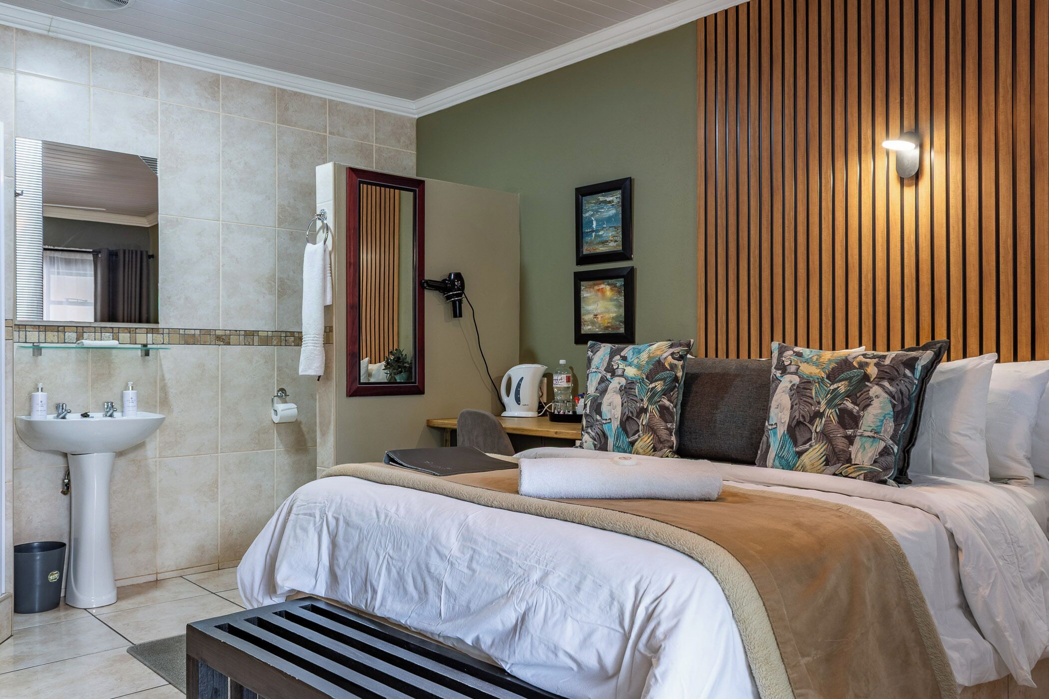 Une chambre d’hôtel comprenant un lit, une table de chevet, un miroir, un lavabo et un espace douche.