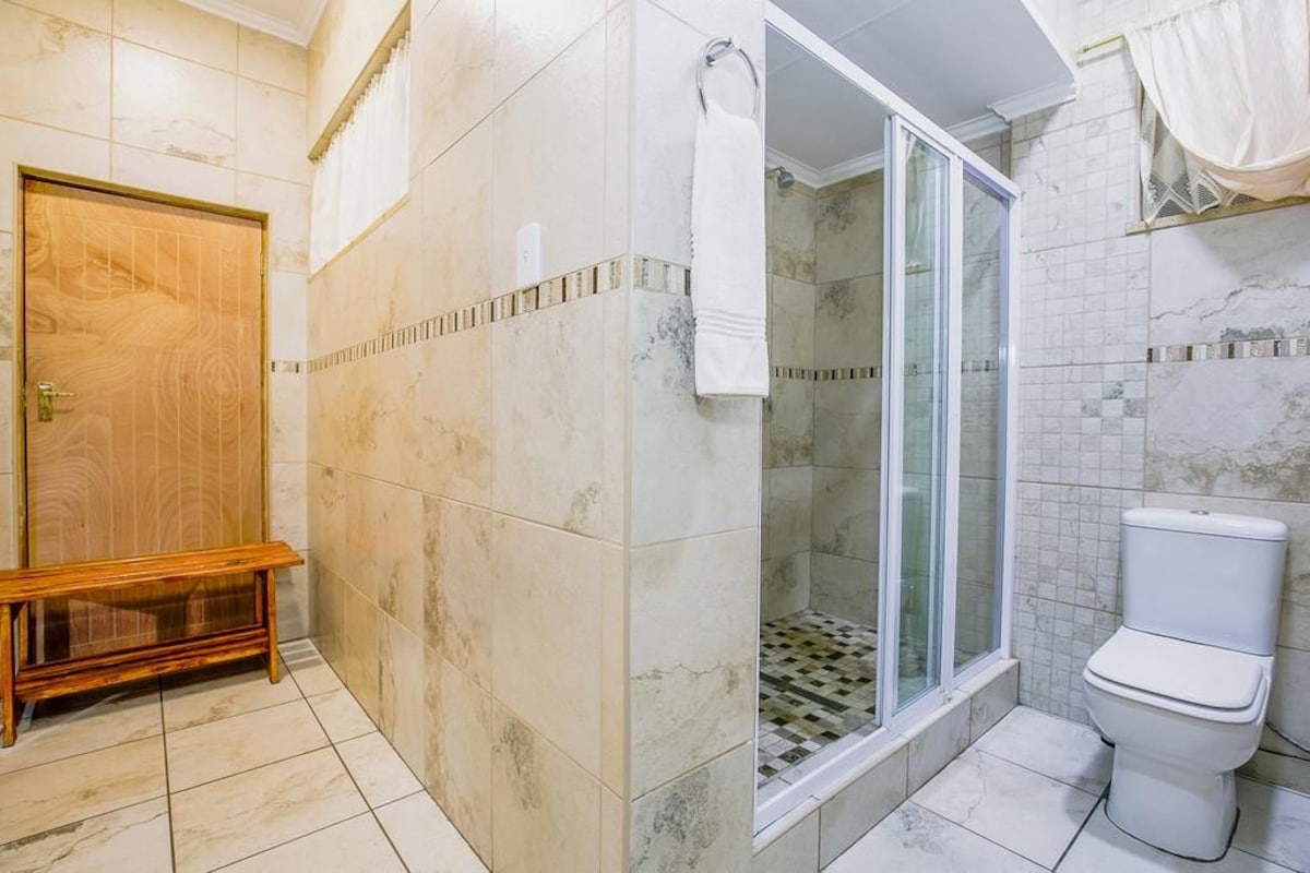 A bathroom with a shower, toilet, bench, and tiled walls.