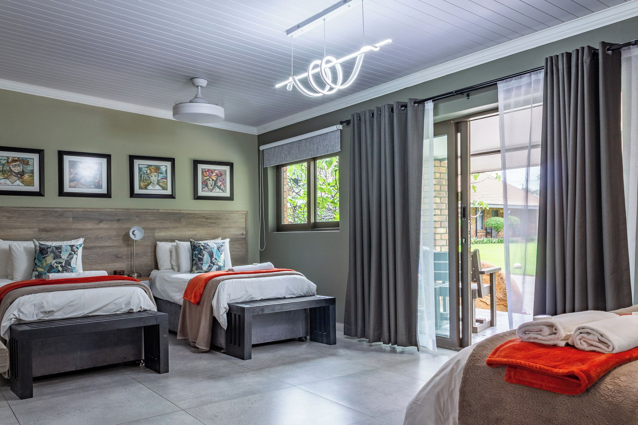 Une chambre moderne avec deux lits, un banc et un luminaire suspendu au plafond.