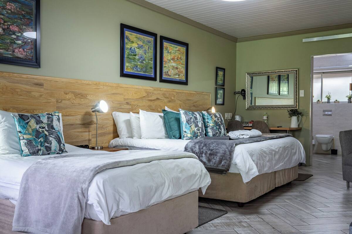 A hotel room with two beds, a wooden headboard, a large mirror, and artwork on the walls.