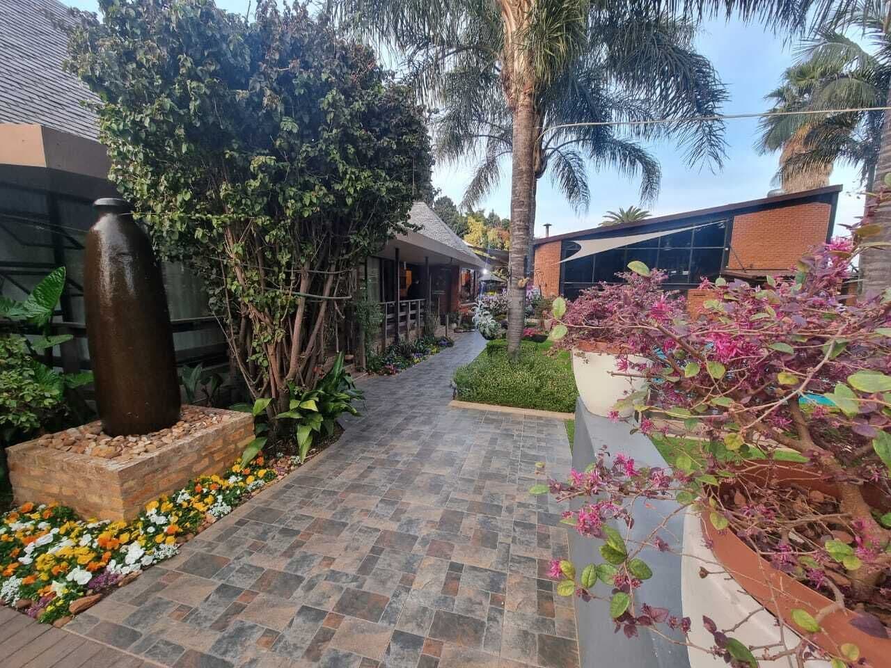 A pathway leading to a building with a modern design, surrounded by lush greenery and flowering plants.