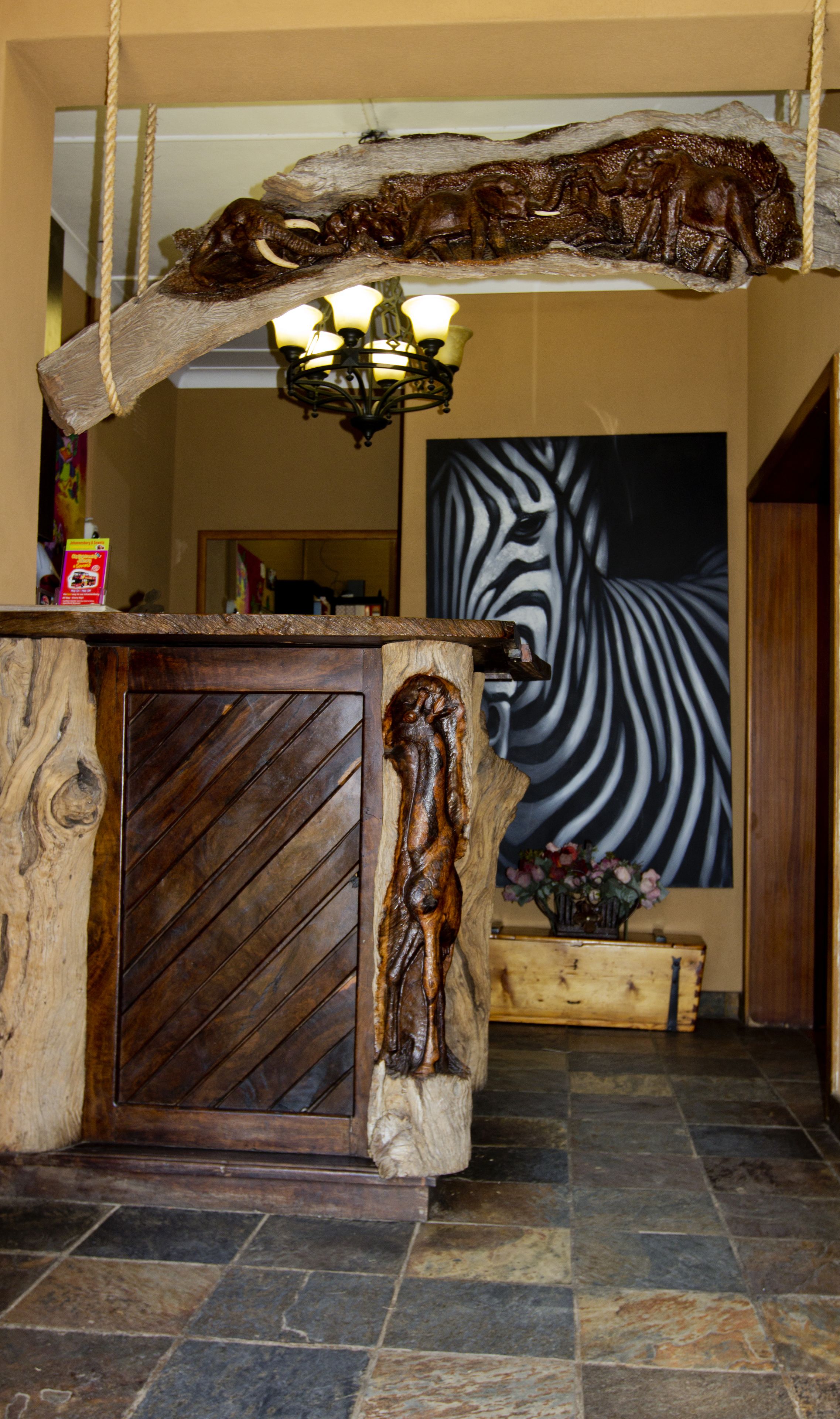 A reception desk with a rustic design, featuring a large wooden sculpture, a chandelier, and a zebra painting in the background.