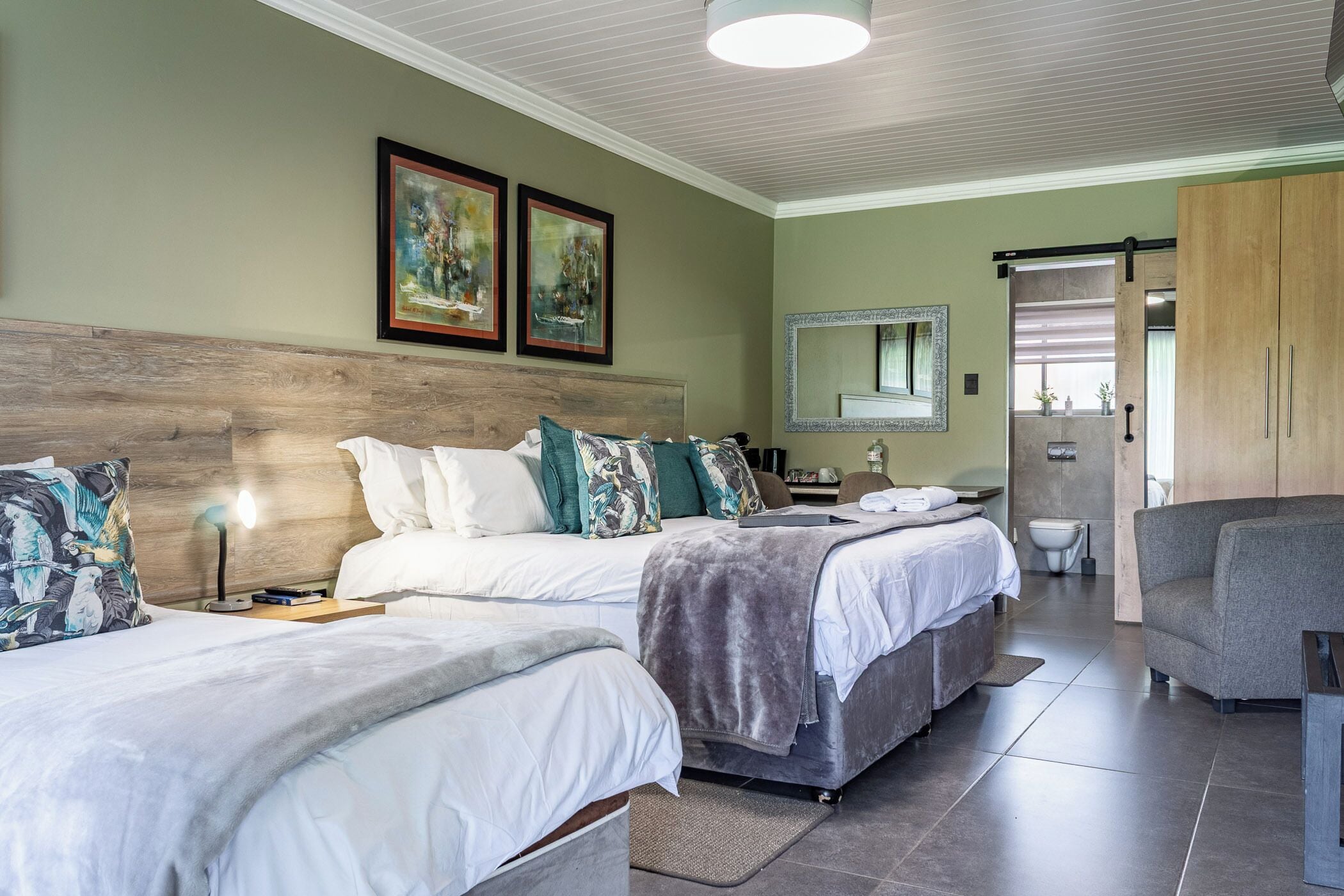 A hotel room with two beds, a large mirror, a wardrobe, and a seating area.