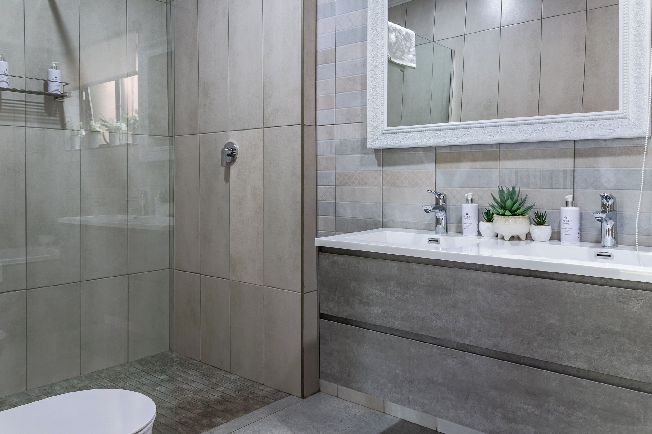 A modern bathroom with a glass shower enclosure, a white sink with a mirror above, and toiletries on the countertop.