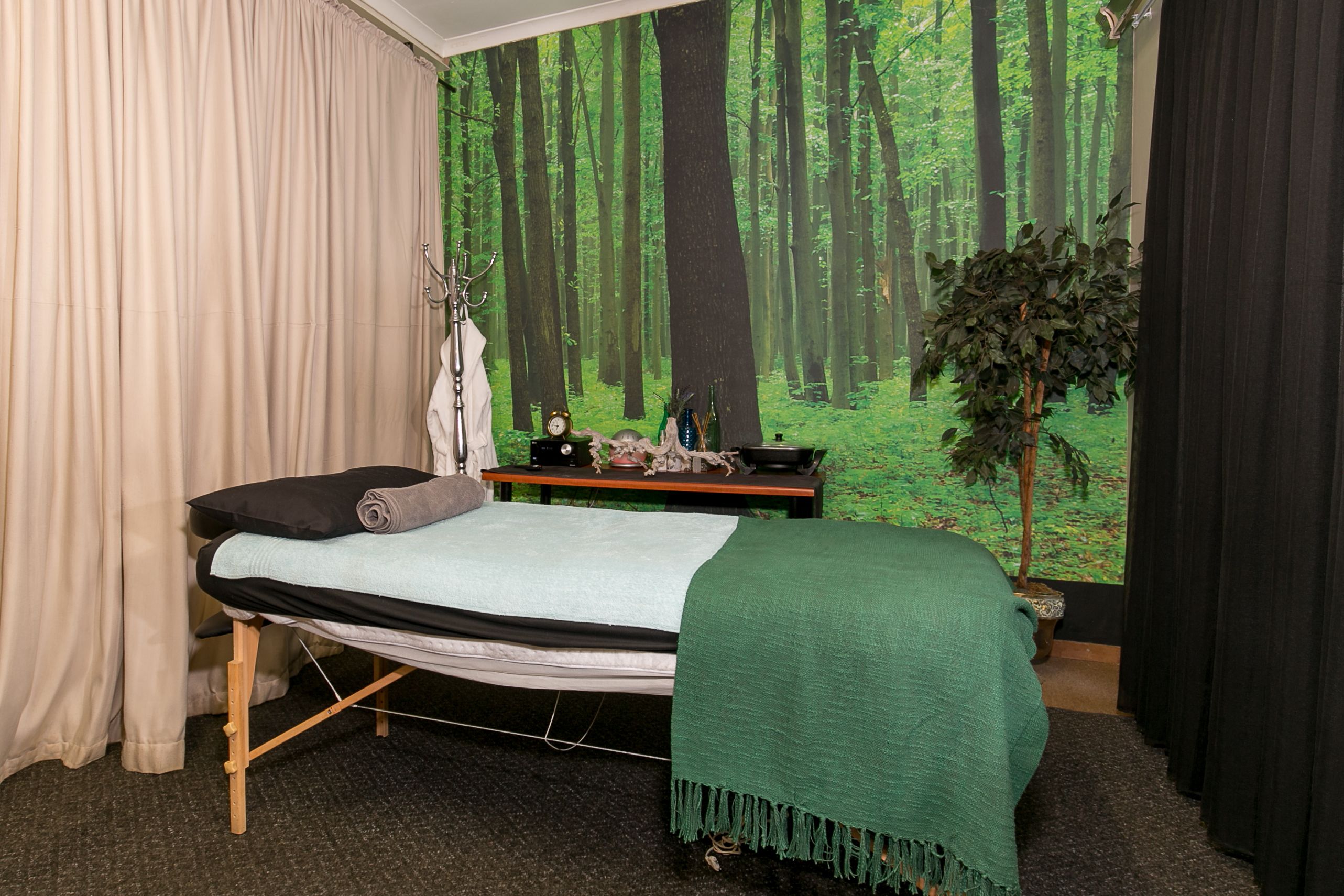Ein Zimmer mit einem Bett, einem kleinen Tisch mit einer Pflanze und einem Wandgemälde von einem Wald.