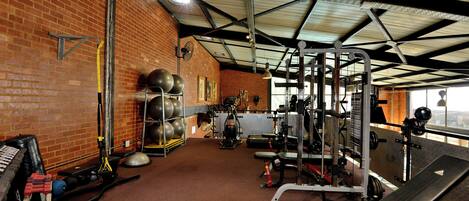 Un gimnasio con diverso equipo de ejercicio, un muro de ladrillo y un techo metálico.