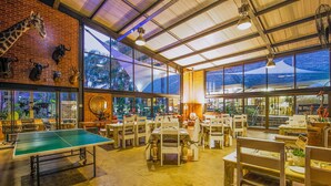 A spacious indoor area with a ping pong table, multiple dining tables, chairs, and a brick wall with mounted animal heads. - Sunrock Guesthouse (Kempton Park)