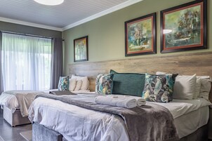 Habitación de hotel con una cama grande, dos camas más pequeñas, un cabecero de madera y obras de arte en las paredes.