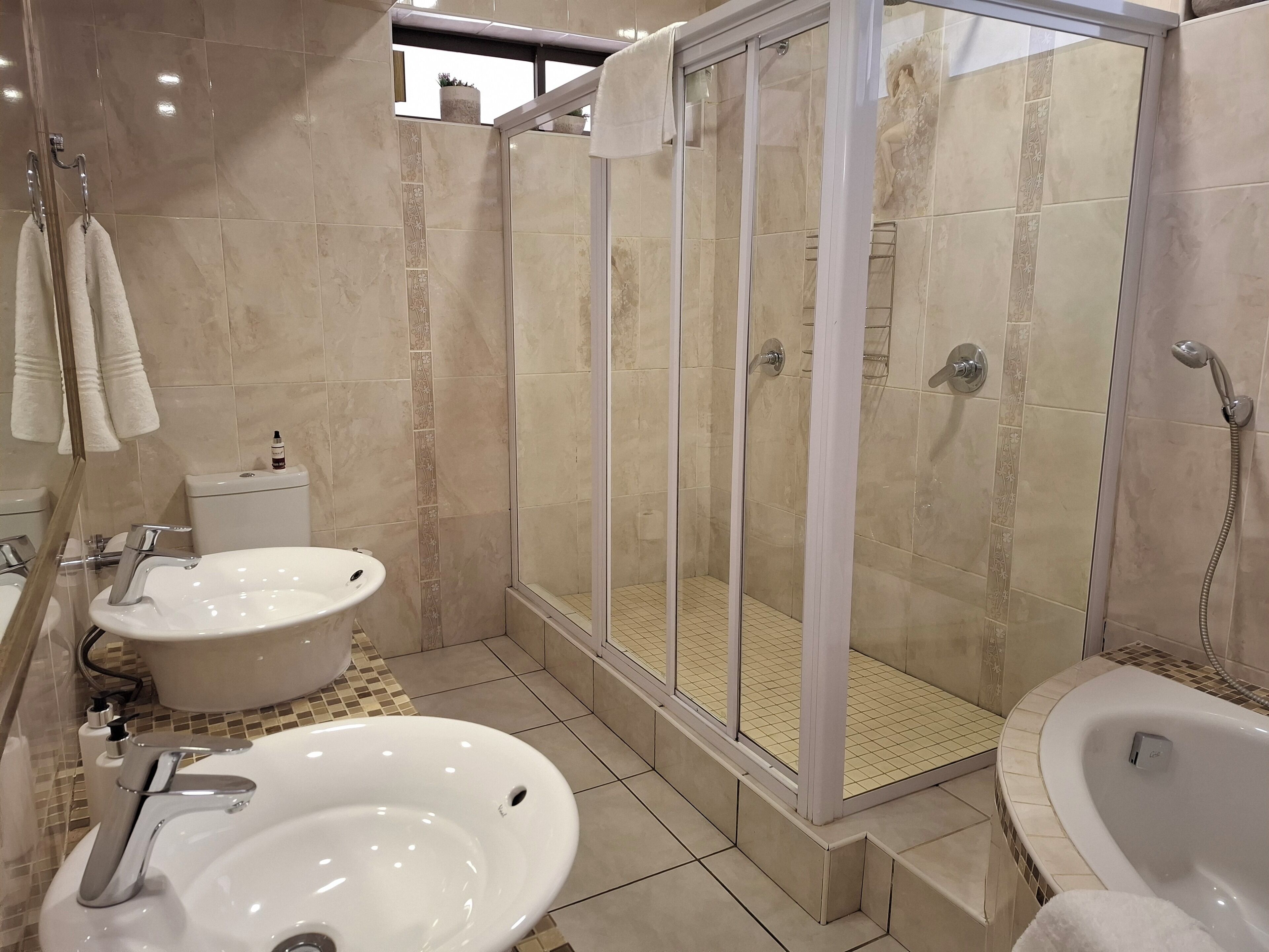 A modern bathroom with a glass-enclosed shower, two sinks, and a bathtub.