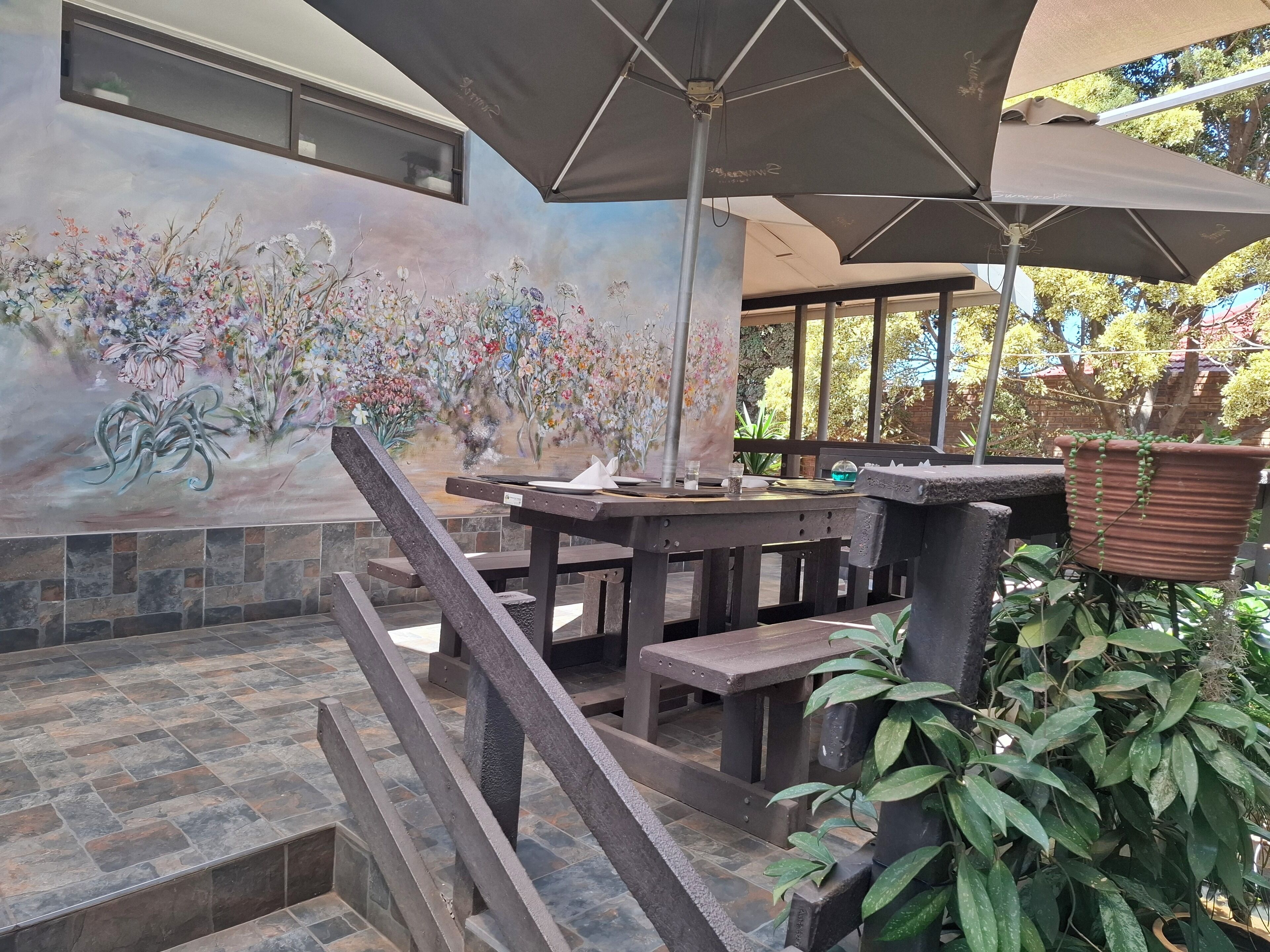 A patio area with a mural of flowers, outdoor seating, and a stone-tiled floor.