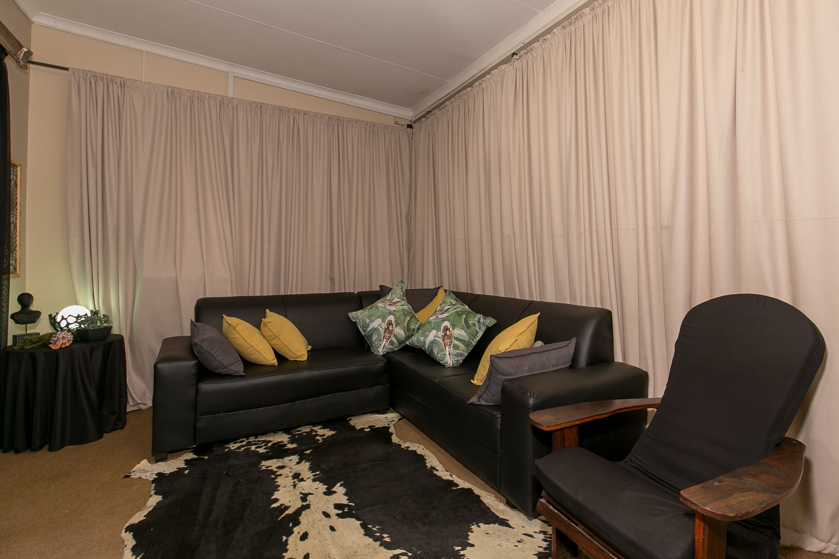 A living room with a black leather sofa, a wooden armchair, and a black and white cowhide rug.