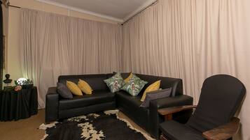 A living room with a black leather sofa, a wooden armchair, and a black and white cowhide rug.