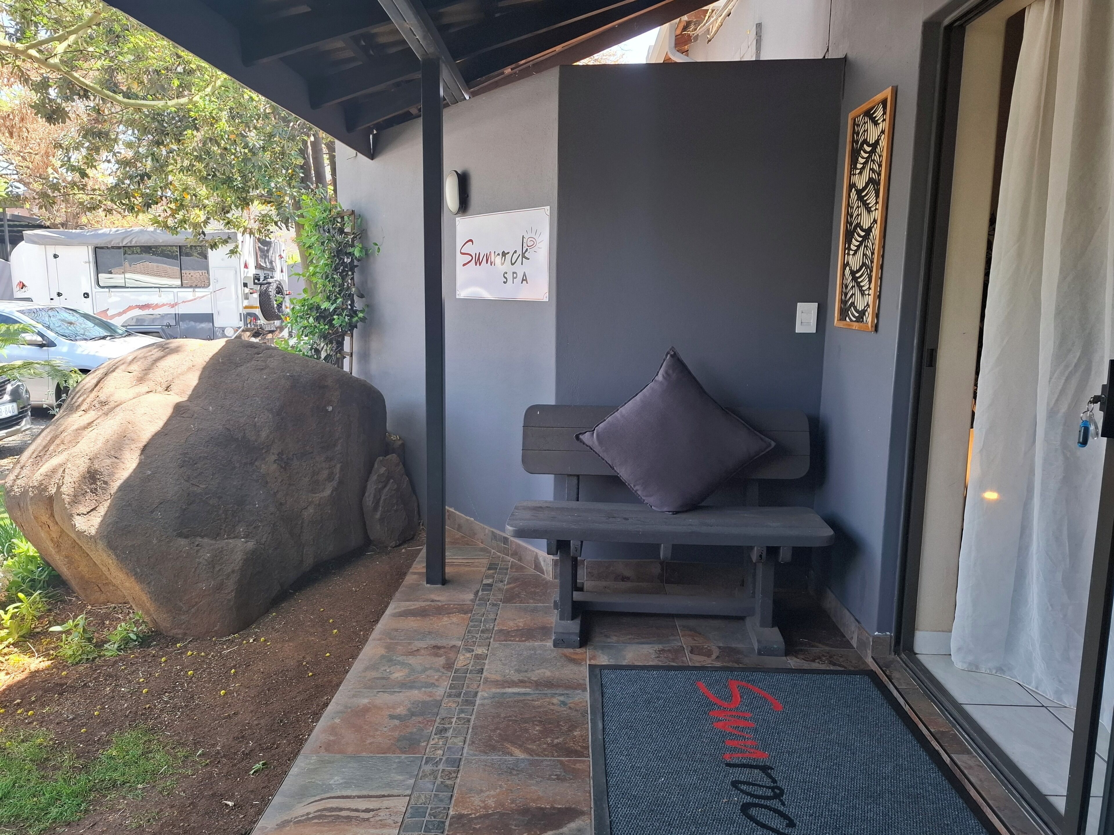 L’entrée d’un spa, avec un banc en pierre, un grand rocher et une enseigne indiquant « Sunrock SPA ».