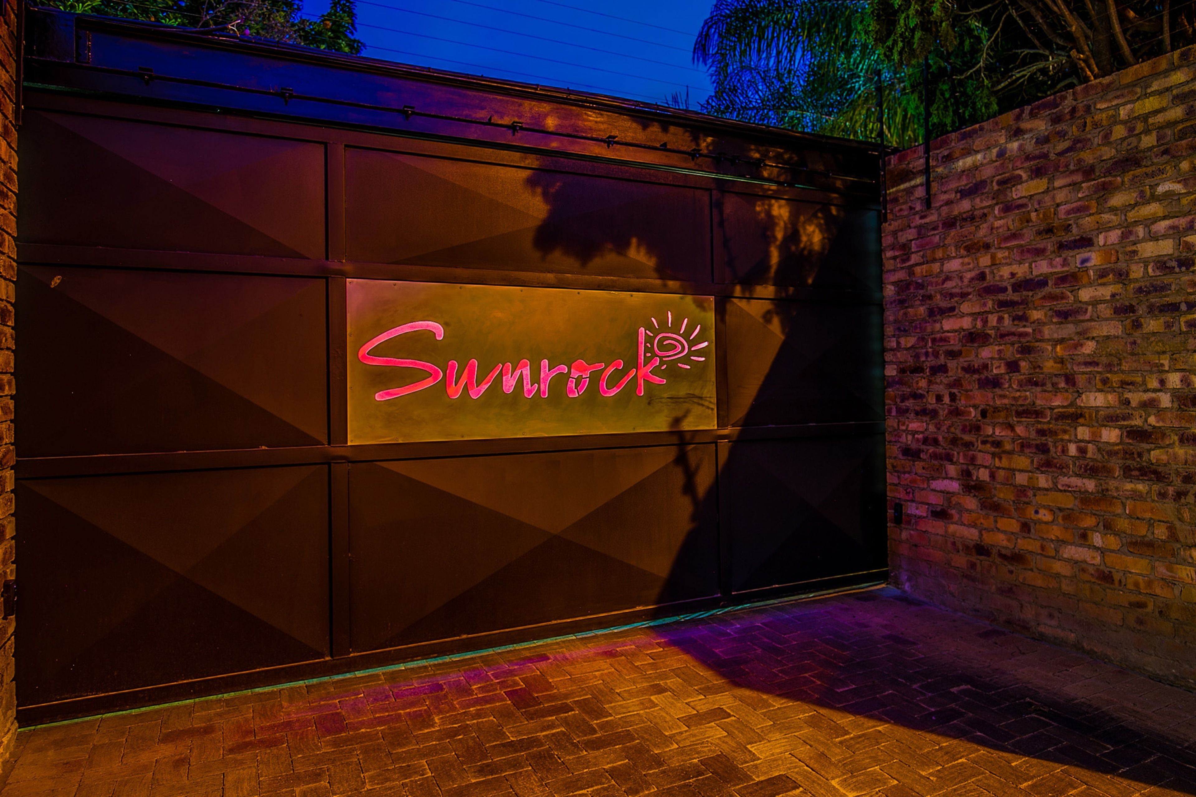 A garage door with the neon sign "Sunrock" and a brick wall to the right.