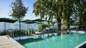 A swimming pool with a wooden deck, lounge chairs, and umbrellas. - Seerose Resort & Spa (Meisterschwanden)