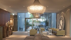 A modern lobby with a large chandelier, wicker furniture, and a large wall clock. - Seerose Resort & Spa (Meisterschwanden)