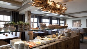 A buffet setup with various food items, a glass display case, and a unique wooden light fixture. - Seerose Resort & Spa (Meisterschwanden)