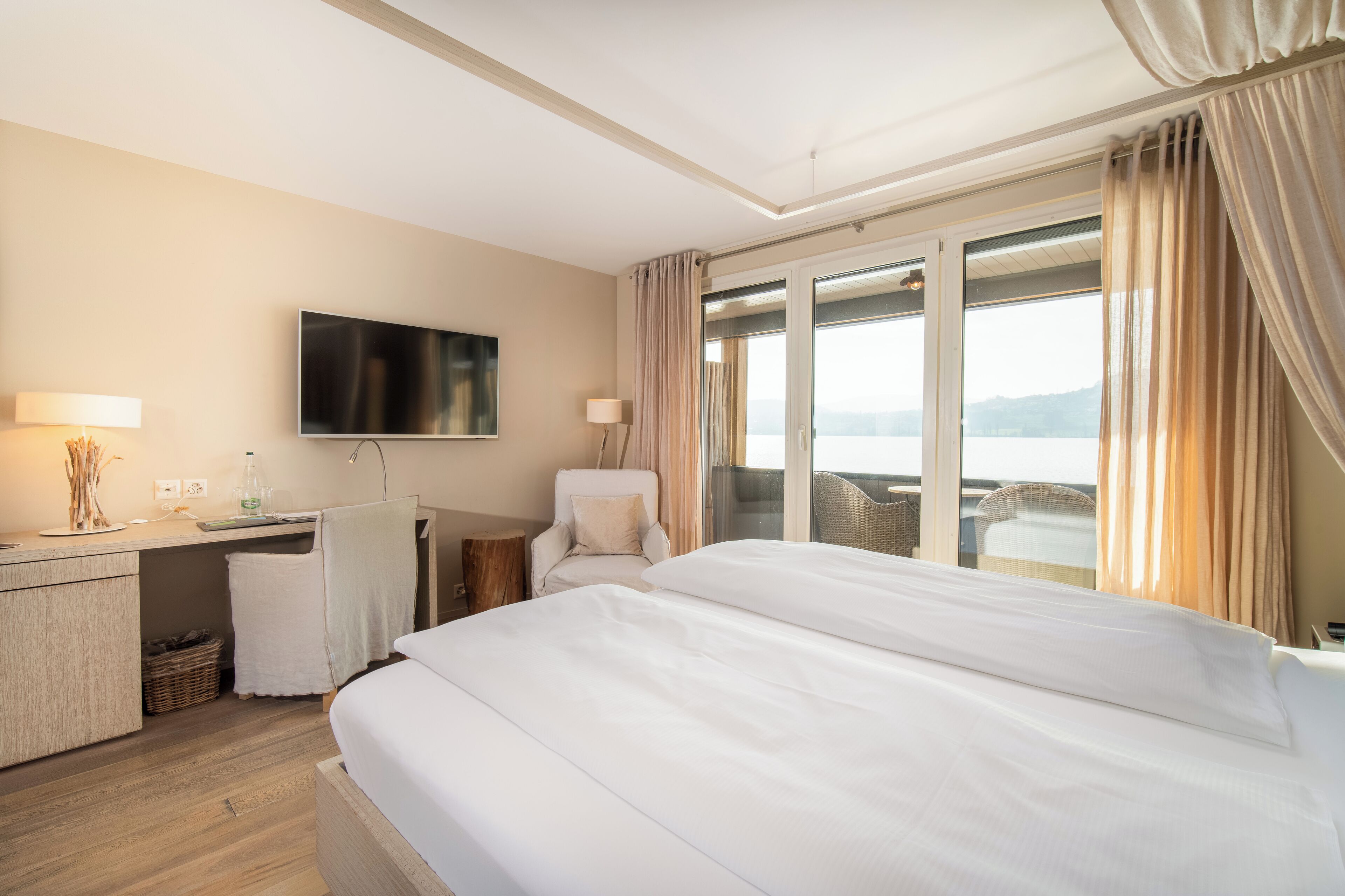 Une chambre d’hôtel avec un grand lit, un bureau doté d’une télévision à écran plat, une chaise et une vue sur la mer.