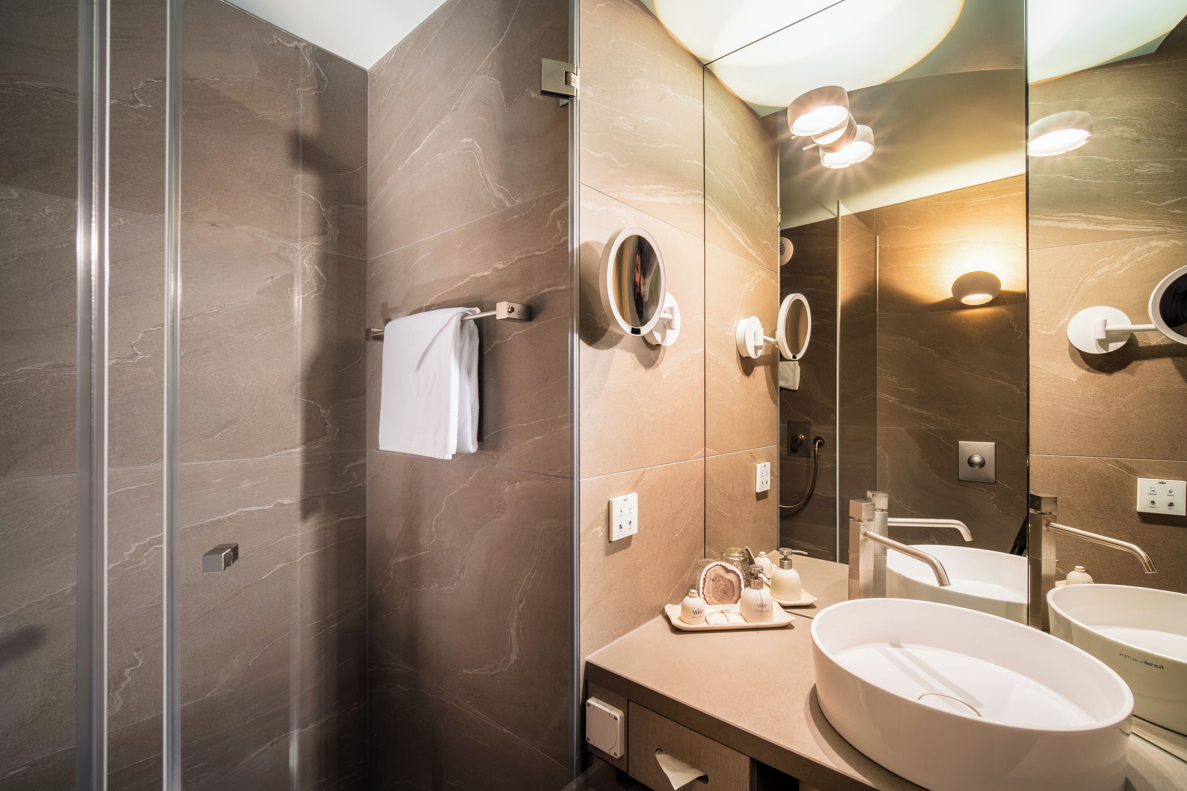 A modern bathroom with a glass shower enclosure, a vanity with two sinks, and a large mirror.