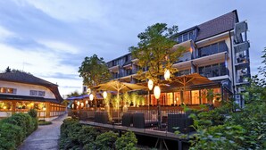 A hotel with outdoor seating, a covered patio, and a pathway leading to the entrance. - Seerose Resort & Spa (Meisterschwanden)